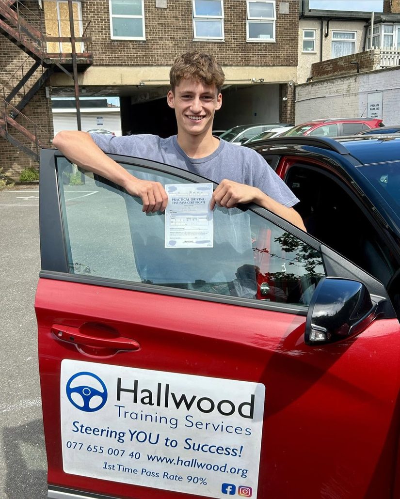 Newly passed driver leaning on the door of the Hallwood Training Services car with its Steering You to Success sign