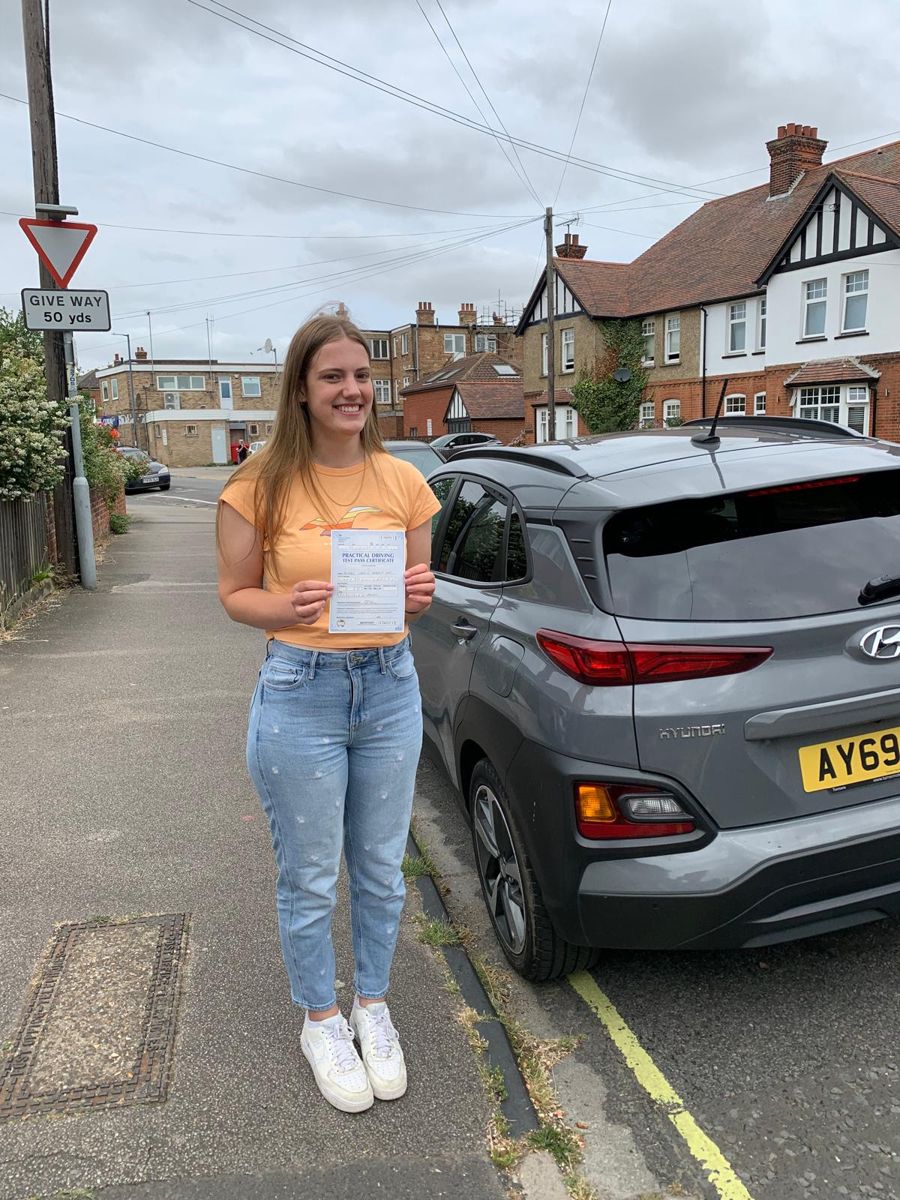 Learner driver standing on the pavement beside a car, holding her driving test pass certificate