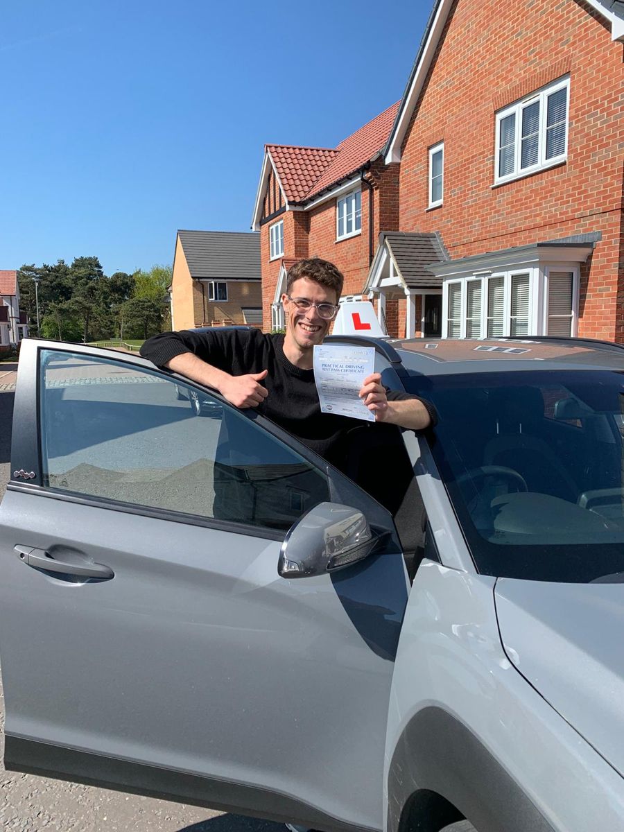 Learner driver giving a thumbs up with his pass certificate, leaning on the car door