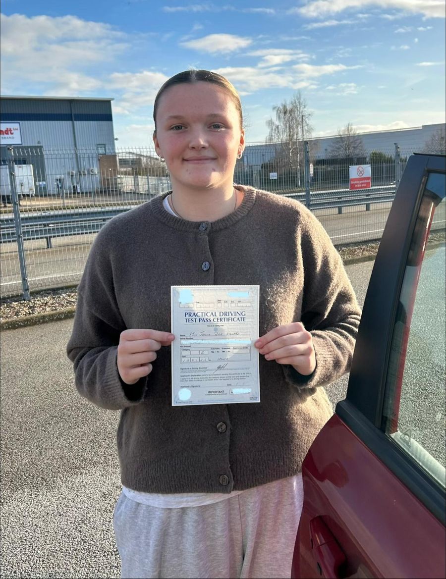Learner holding her pass certificate in both hands beside the car on a sunny day