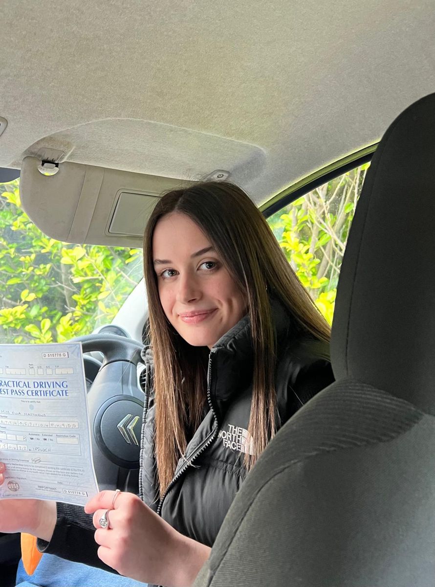 New driver sitting in the car holding her practical driving test pass certificate