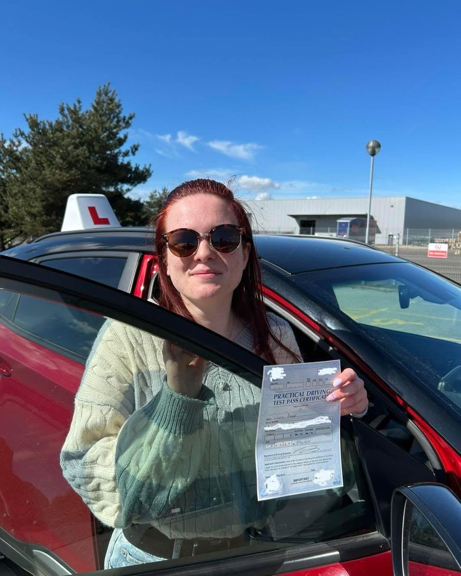 New driver in sunglasses holding up her pass certificate by the Hallwood Training Services car