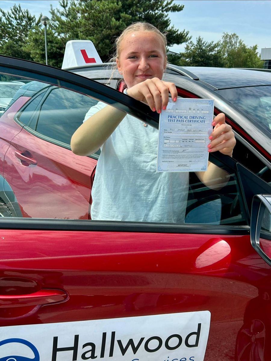 Pupil leaning out of the red Hallwood Training Services car holding her driving test pass certificate