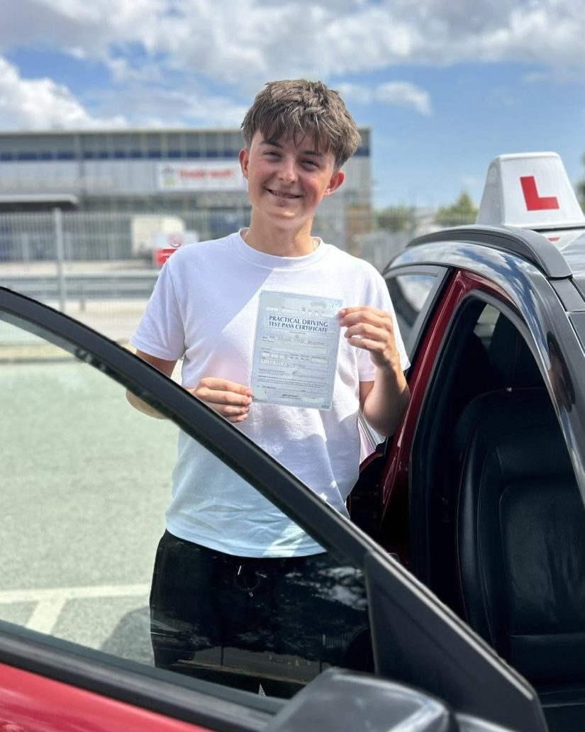 Teenage learner smiling with his pass certificate beside the Hallwood Training Services car at Ipswich test centre