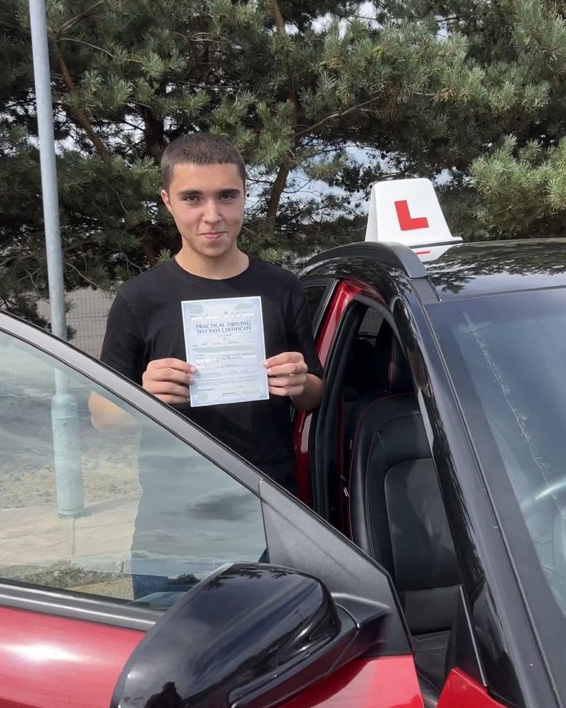 Young driver standing by the open door of the Hallwood Training Services car with his pass certificate